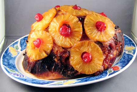 ham covered in pineapples and maraschino cherries on a tastefully elegant plate