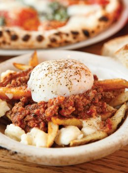 A poached egg sits atop an Italian version of poutine with Bolognese subbing for gravy. 