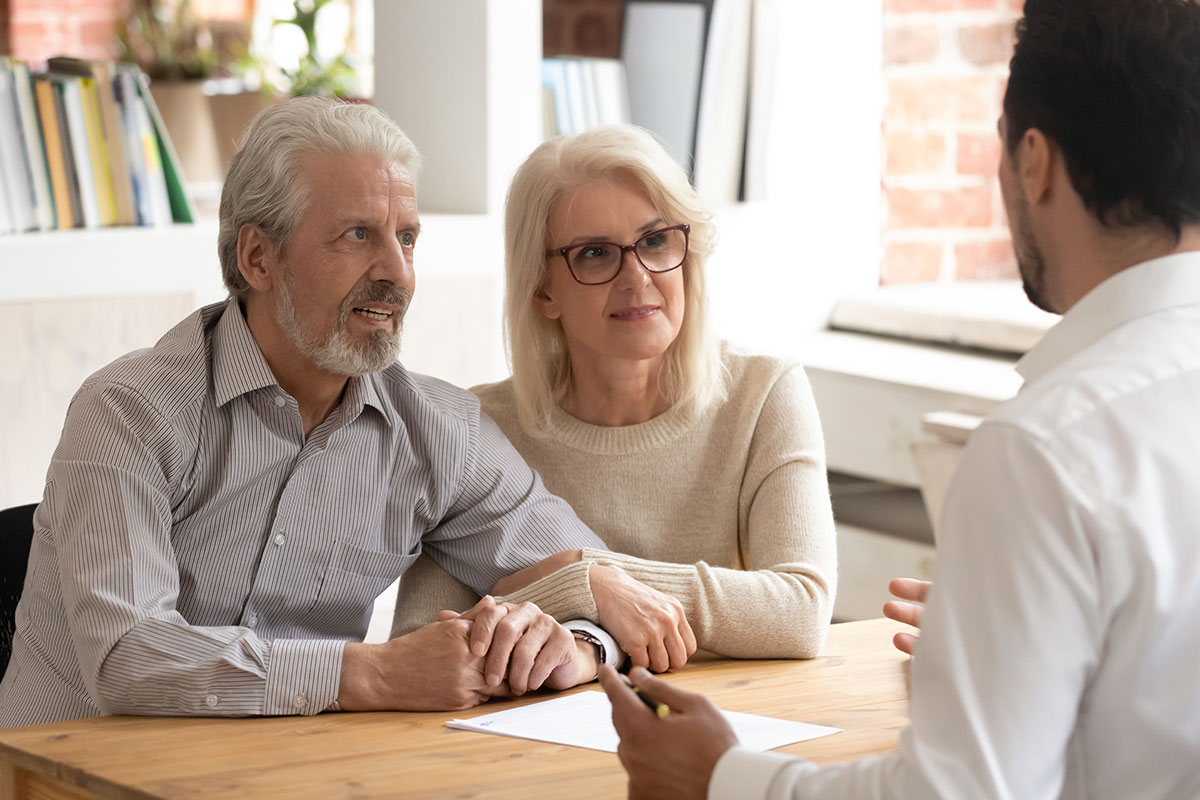 elderly couple talking to man at desk