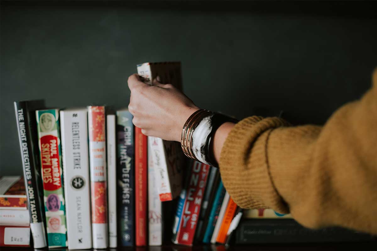 woman putting book on shelf with stack of books