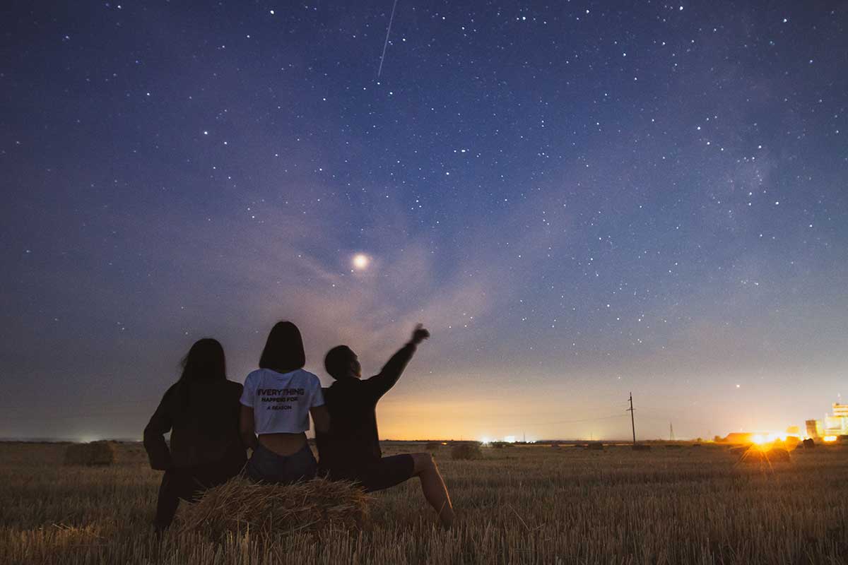 three people stargazing with blue sky and stars