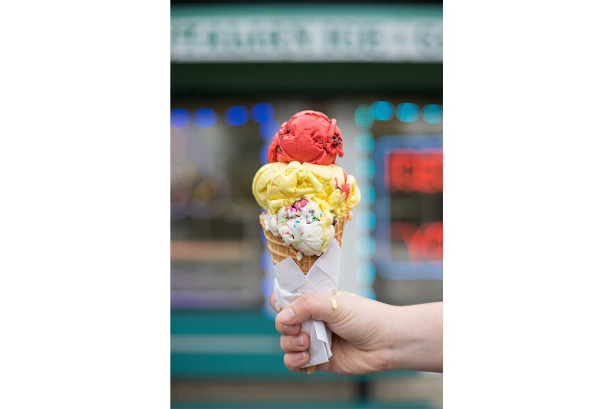 person holding cone of ice cream with white yellow and red ice cream flavors